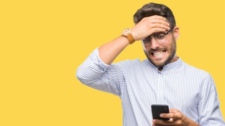 A man wearing a shirt and glasses look down with despair at his phone, which he is holding. 
