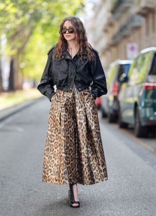 A guest wears black sunglasses, a black leather biker jacket, a brown leopard print skirt, outside Dolce Gabbana, during the Milan Fashion Week Menswear Spring/Summer 2025 on September 21, 2024 in Milan, Italy