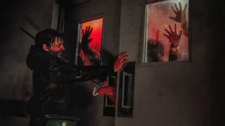 A man barricades himself behind a door while bloodied handprints are visible on the other side