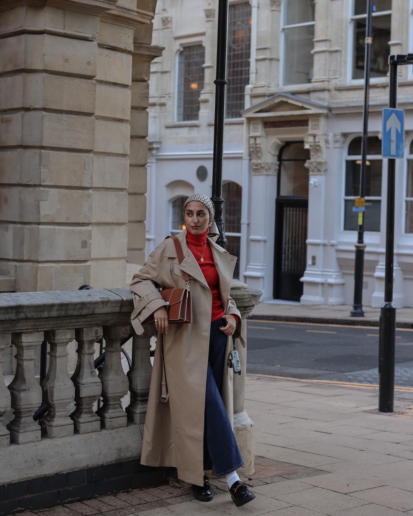 Woman wears trench coat, blue jeans, red roll neck and loafers