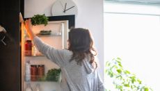 Woman taking bunch of herbs from top shelf of a fridge