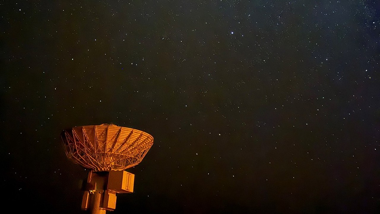 a radar dish is illuminated red against a starry night sky