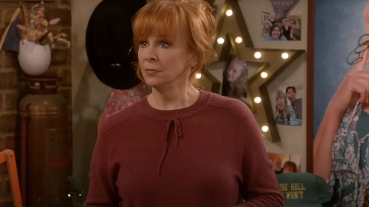 Reba McEntire dressed in a red sweater looking confused in the holiday episode of Happy&#039;s Place