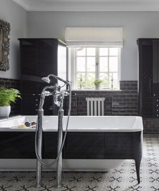 An example of bathroom pictures showing a black bath in the center of a bathroom with mosaic floor tiles and black metro tiles on the wall