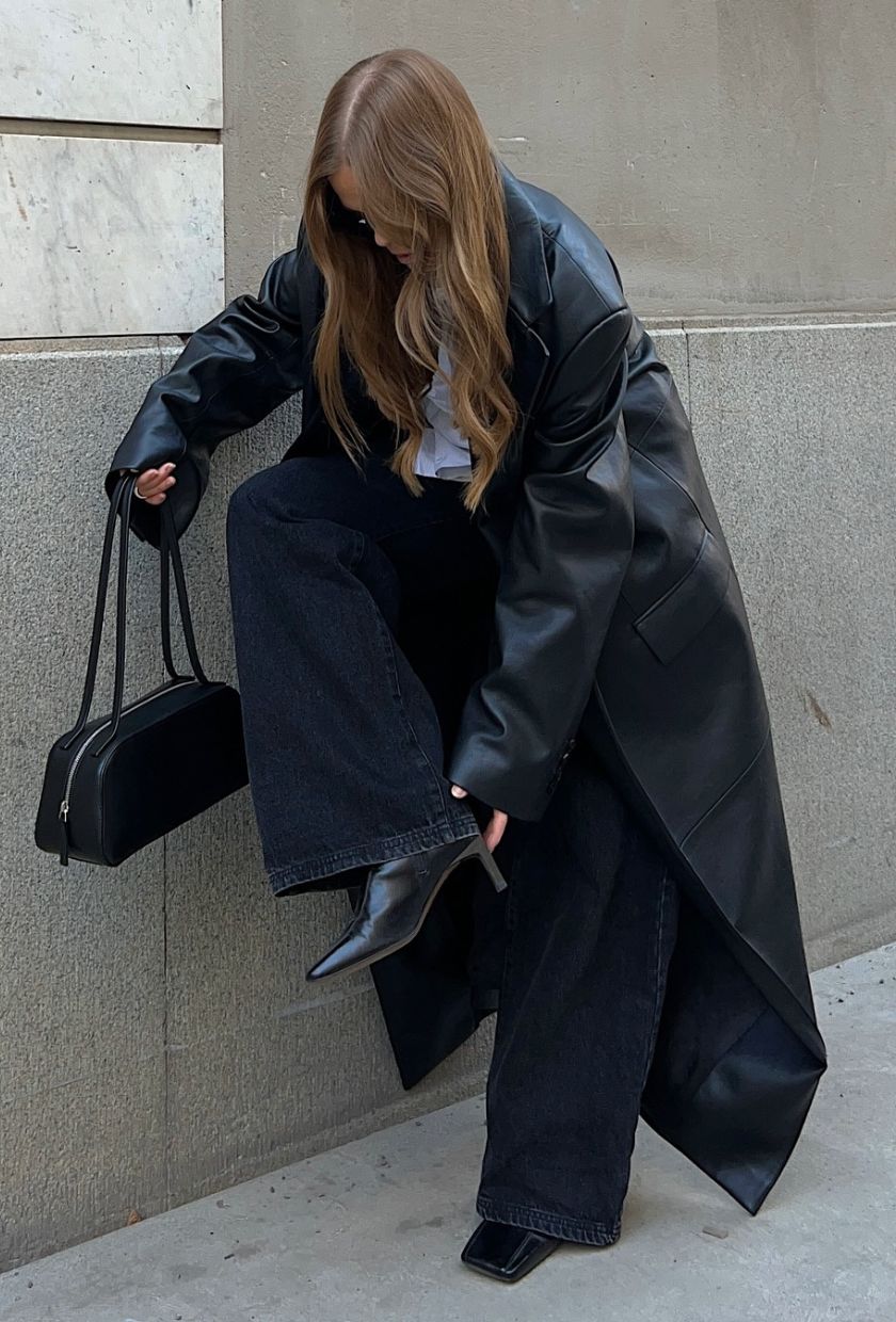 @haaannajohansson wears black baggy jeans, with a leather trench, white top, black kitten-heel boots and black bowling bag