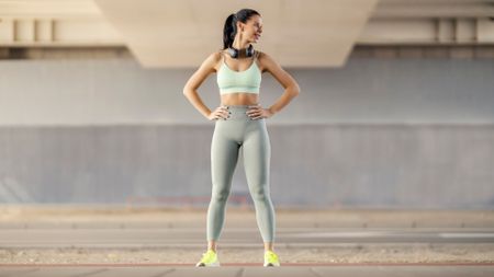 Young woman in activewear standing outdoors with hands on hips smiling