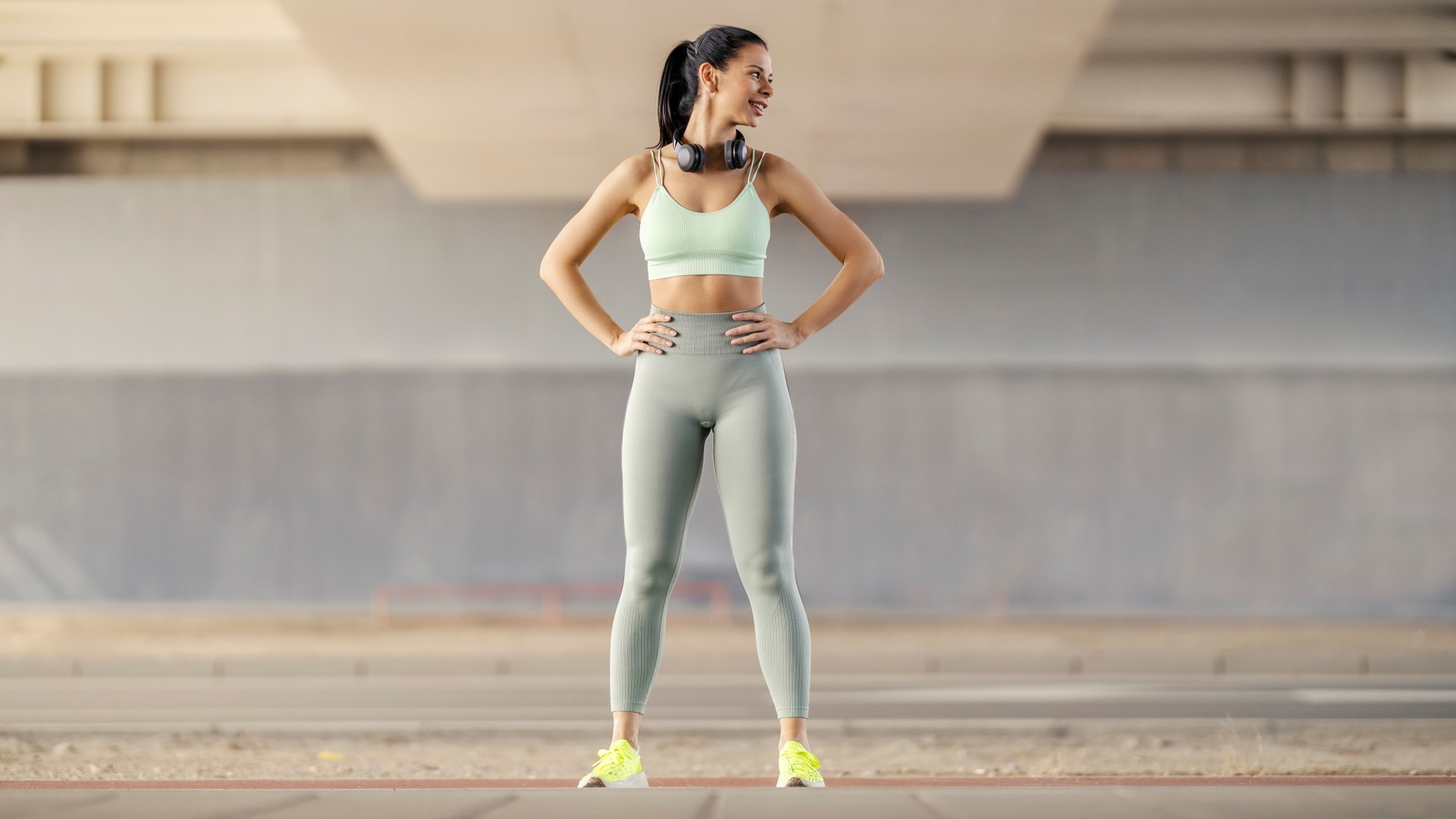 Young woman in activewear standing outdoors with hands on hips smiling