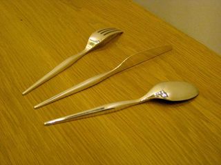 Three silver cutleries (Fork, Knife and Spoon) displayed face down on a wooden surface