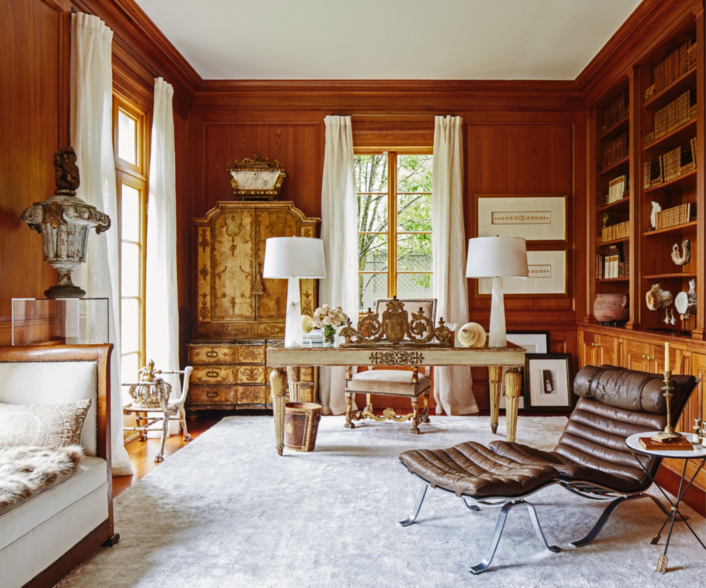 Office with wood panelling and large bookcase, ornate gold desk and wardrobe, midcentury chair and daybed