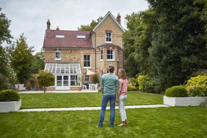 A middle-aged couple look back at a large house from its garden (image: Getty Images)