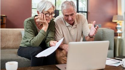 An older couple looks at a laptop together, appearing a bit concerned.