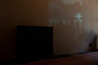 A wall with a black heater radiator next to a wall projection of people standing outside