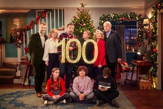 Posed shot of the main cast in festive form in front of a Christmas tree.