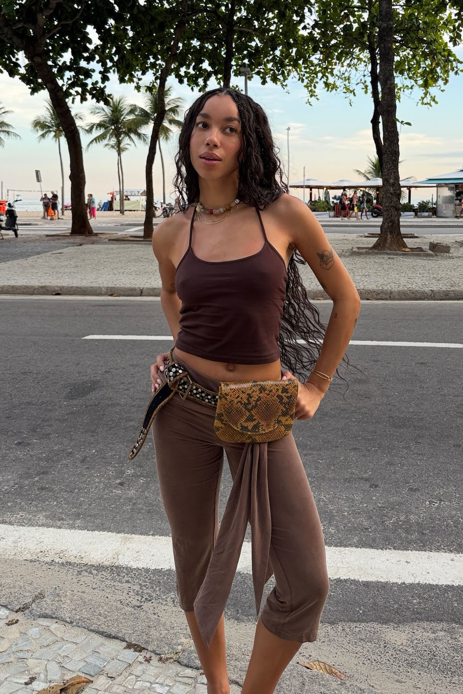 A woman wearing a brown tank top, an animal-print utility belt, and brown capri pants.