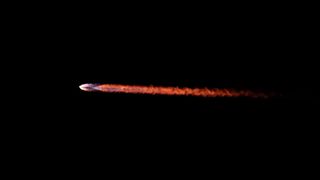 closeup of the trail of flame left by a rocket as it rises into a dark sky