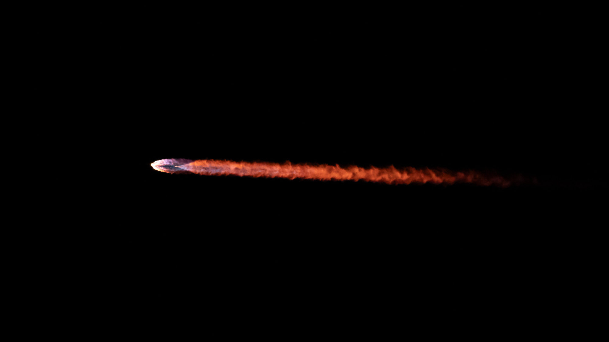 Close-up of the flame trail left by a rocket as it rises into a dark sky