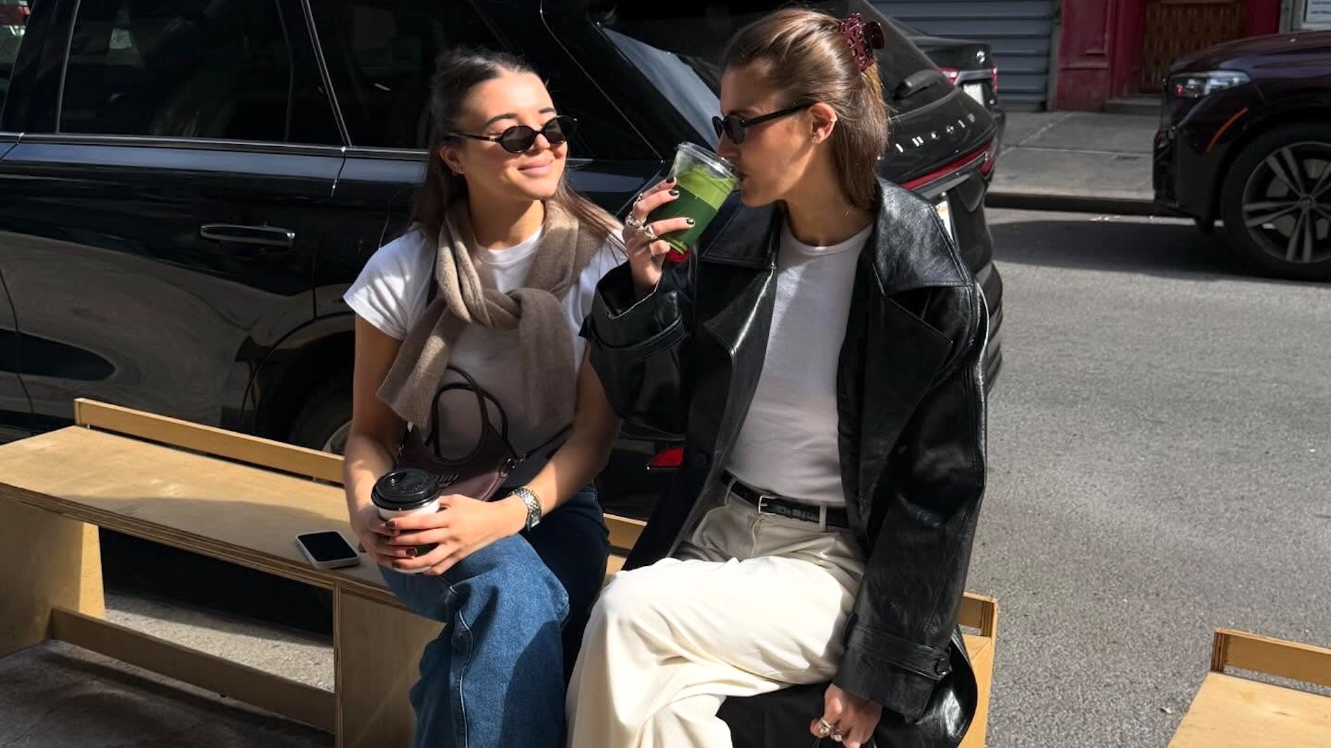 style influencer Coco Schiffer and her sister sit on a sidewalk bench in NYC wearing chic casual outfits with white T-shirts