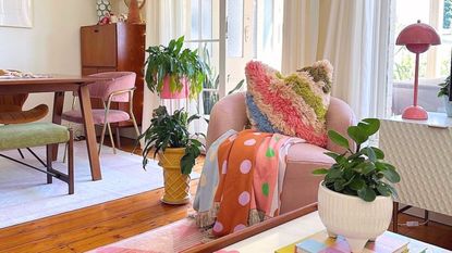 A small living room with a pink chair, plants, and a coffee table