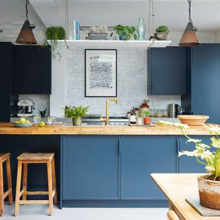 kitchen with dark blue cabinets wooden worktop, wooden stools and white brick wall