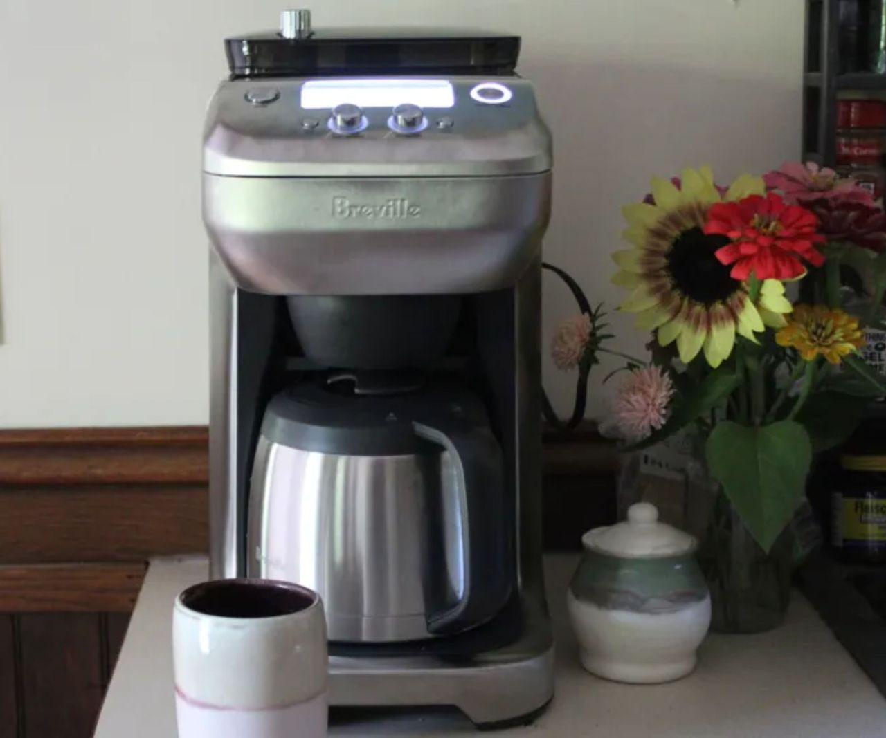 Breville Grind Control Coffee Maker on a countertop with a coffee mug and a vase of flowers
