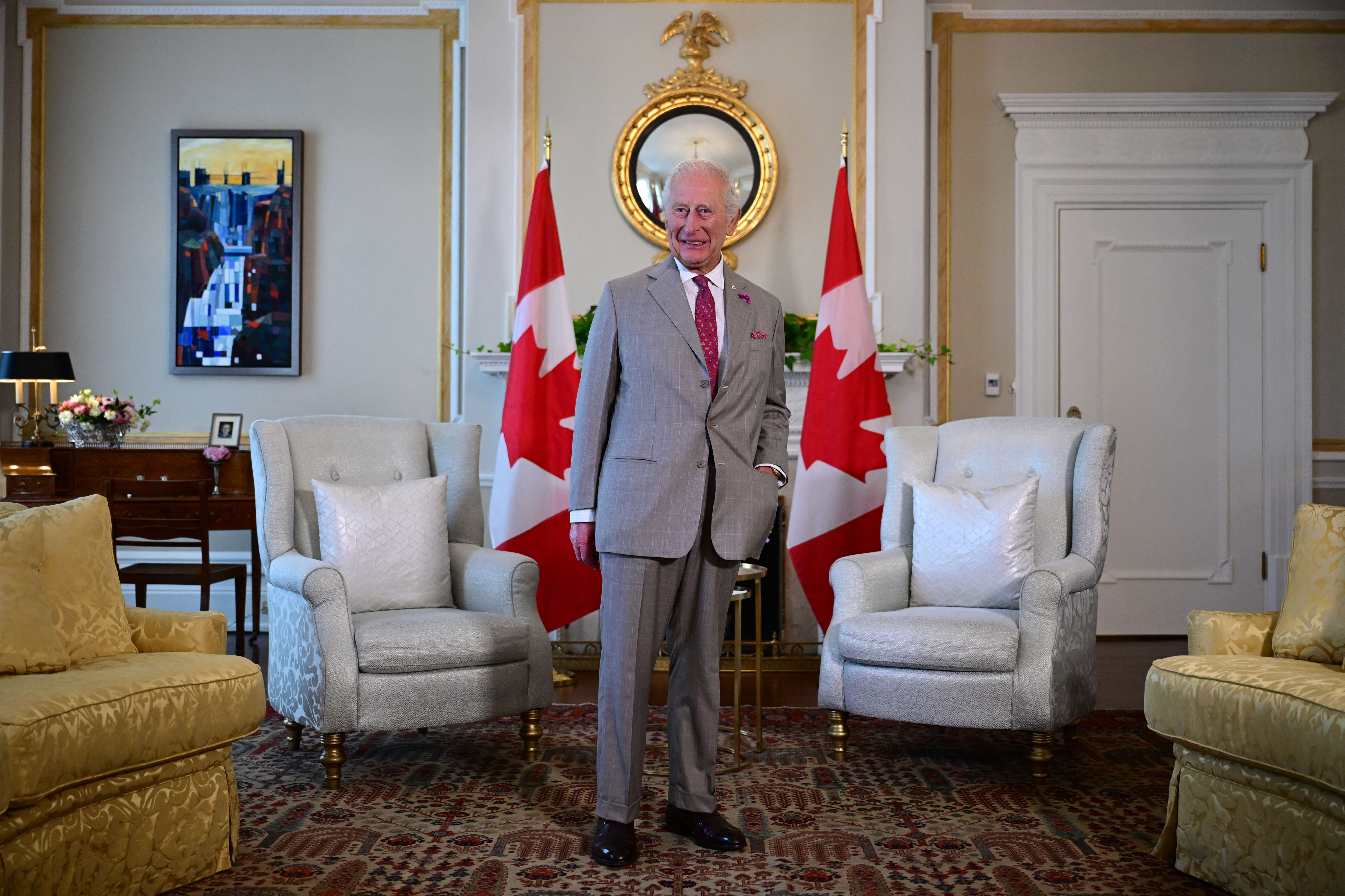King Charles wearing a gray suit in front of two Canadian flags