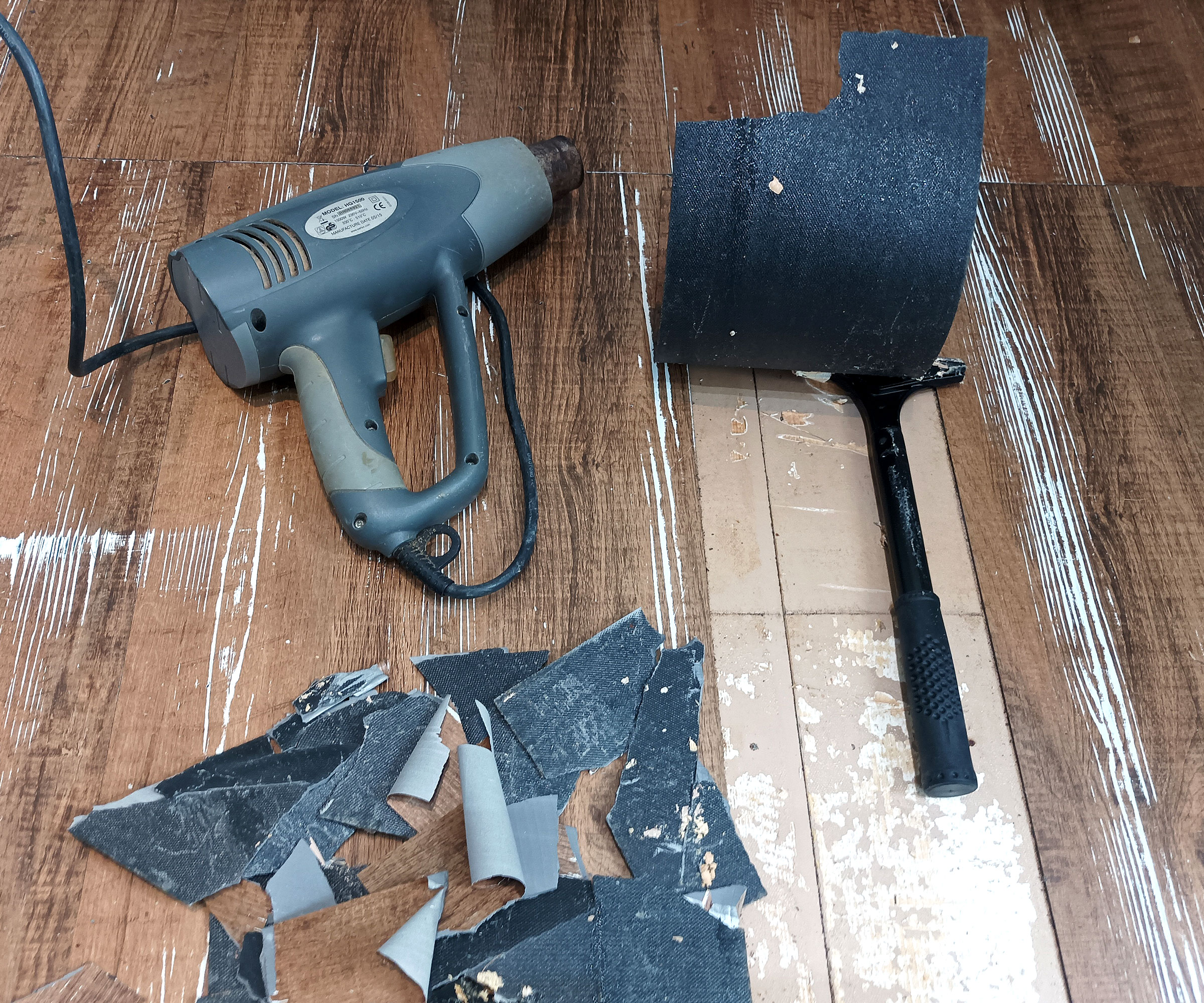 Heat gun and long-handled scraper on worn wood effect vinyl planks with one being removed