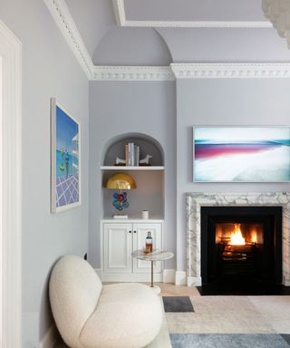 Light blue living room, fireplace, artwork on wall, alcove shelving, low cream curved seat