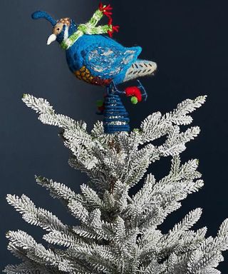 A wool/felt blue ice skating partridge Christmas tree topper on frosted artificial Christmas tree