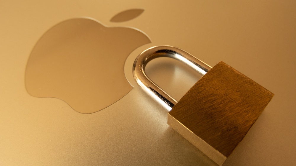 A padlock resting next to the Apple logo on the lid of a gold-colored Apple laptop.