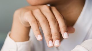 persons hand and chin with plain milky nails