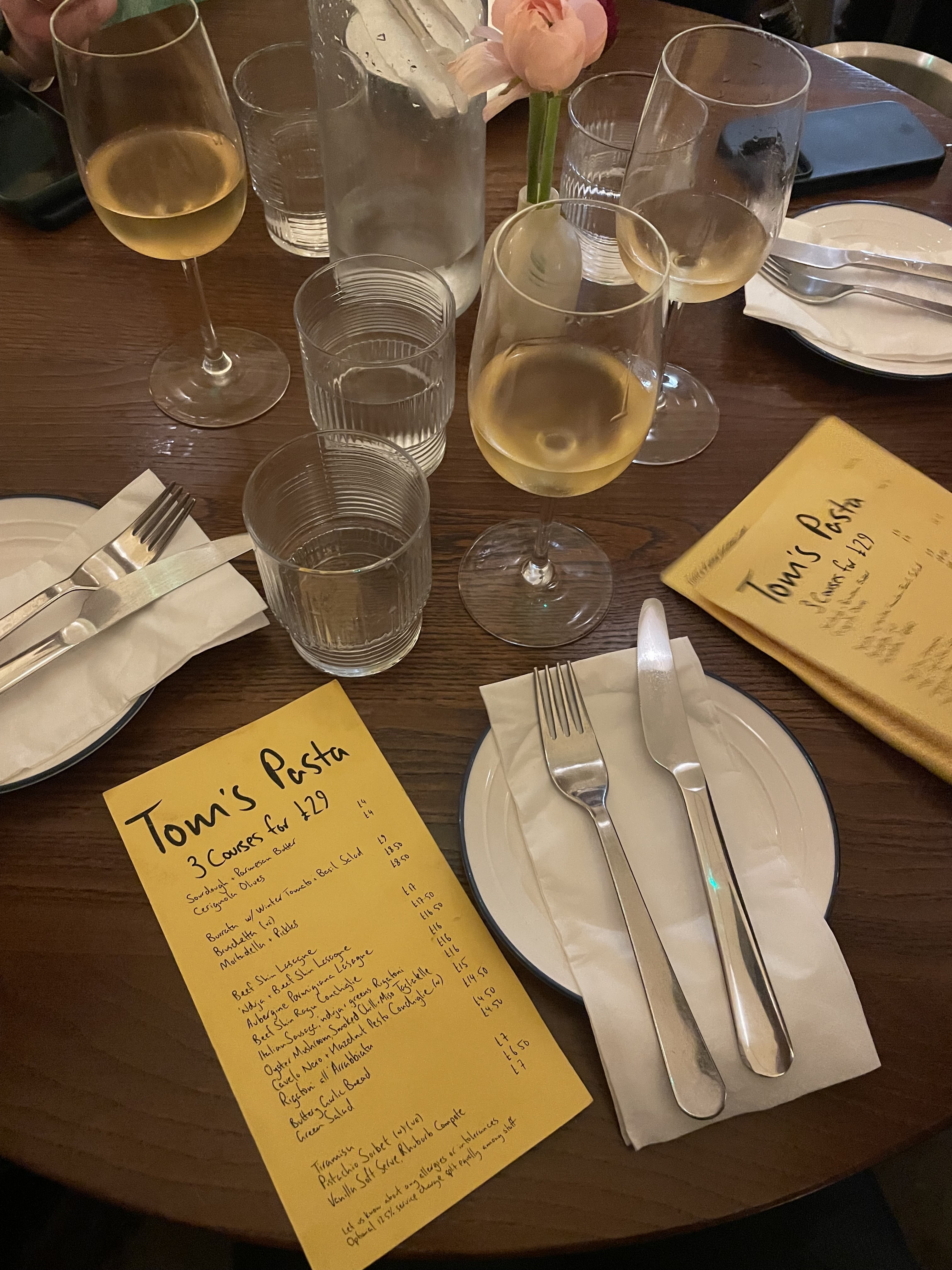 an image of the table at tom's pasta with menus, plates, and fresh glasses of white wine