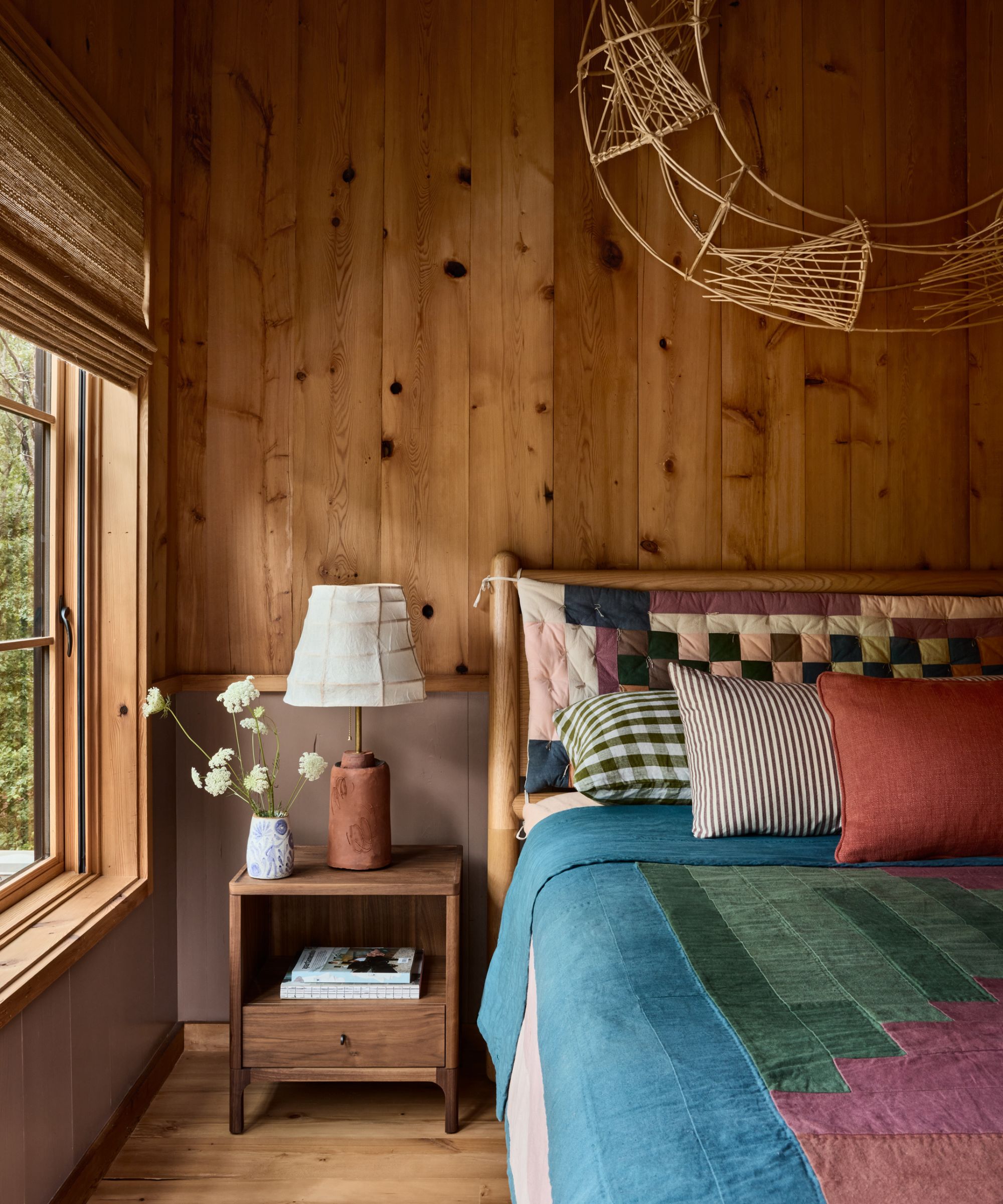 Cozy cabin bedroom with wood plank walls, a colorful patchwork quilt, a small wooden nightstand, and a woven wooden wall hanging
