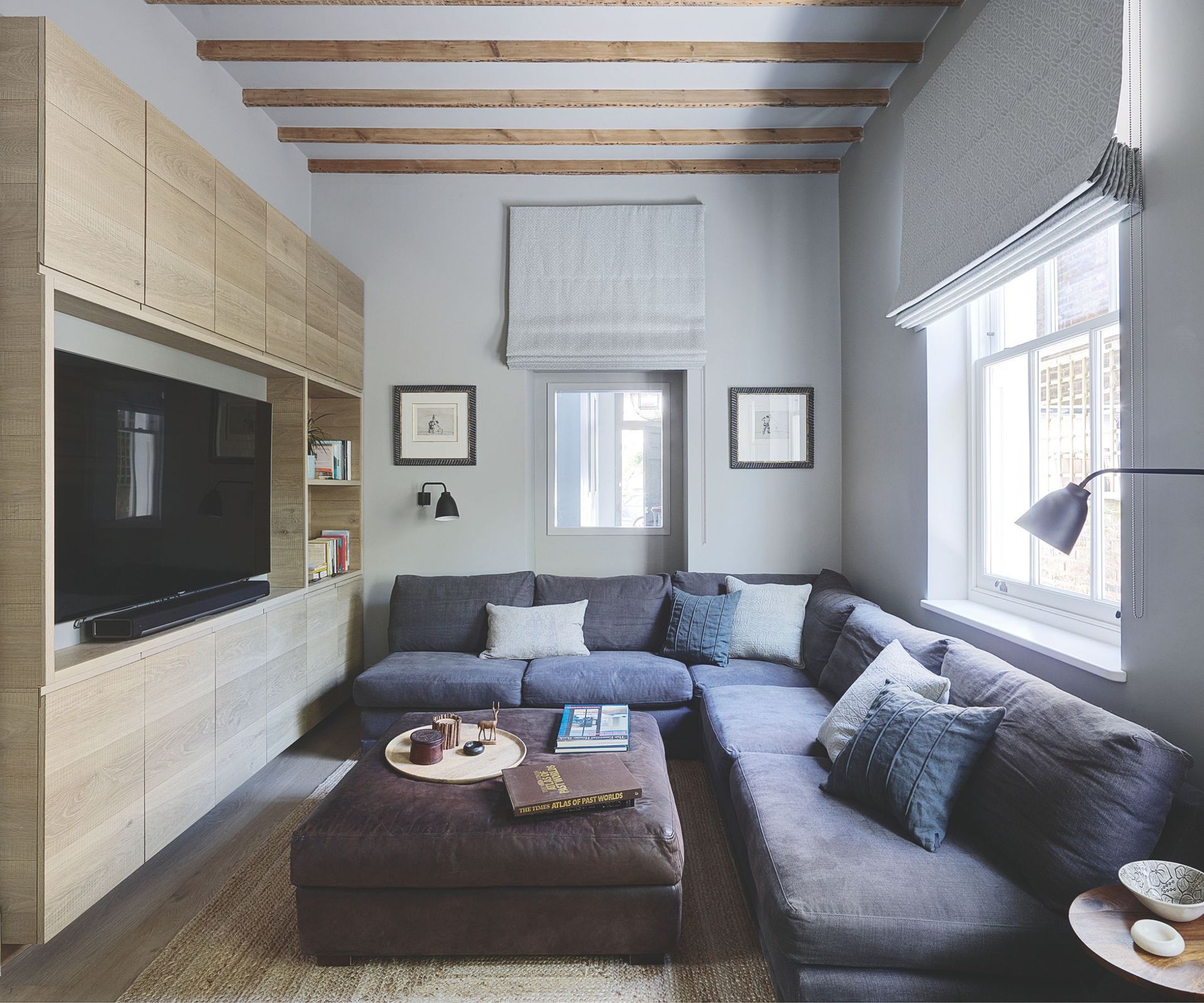 Living room with l shaped sofa, media console with TV, ottoman and beams