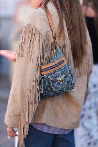 Fashion week guest is seen wearing a brown suede jacket with fringes and a red and blue striped shirt, with a Louis Vuitton bag in blue jeans before Lovechild 1979 show during day two of the Copenhagen Fashion Week