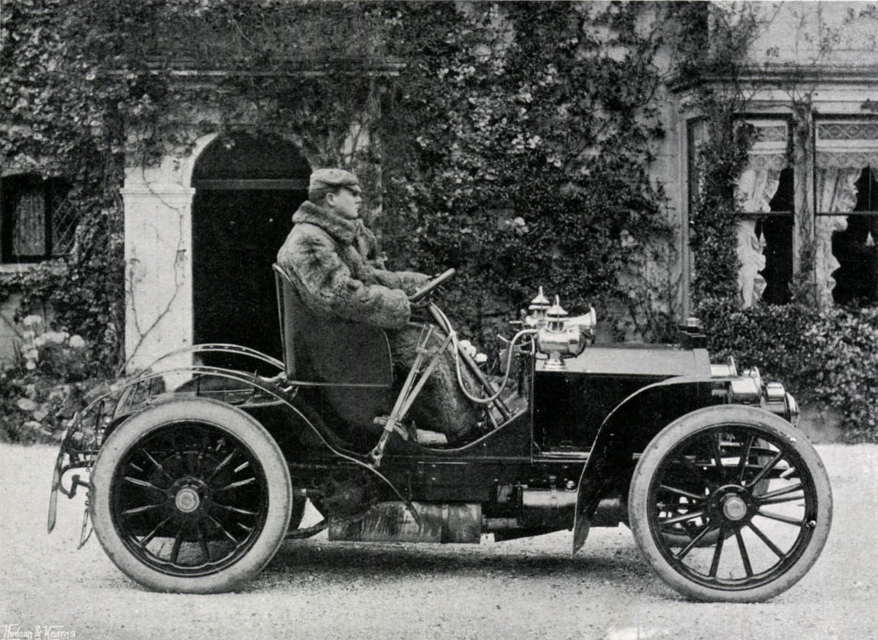Black and white image of a man driving a pre-war car in the 1900s