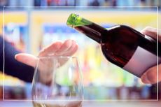Giving up alcohol illustrated by a woman putting her hand over a glass to stop someone pouring wine into it