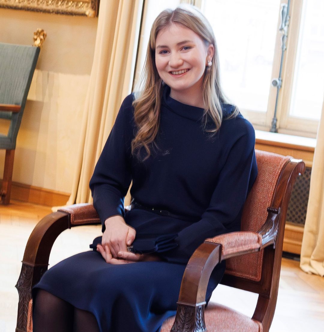 Princess Elisabeth sitting in a chair wearing a blue dress talking to a group of men and women