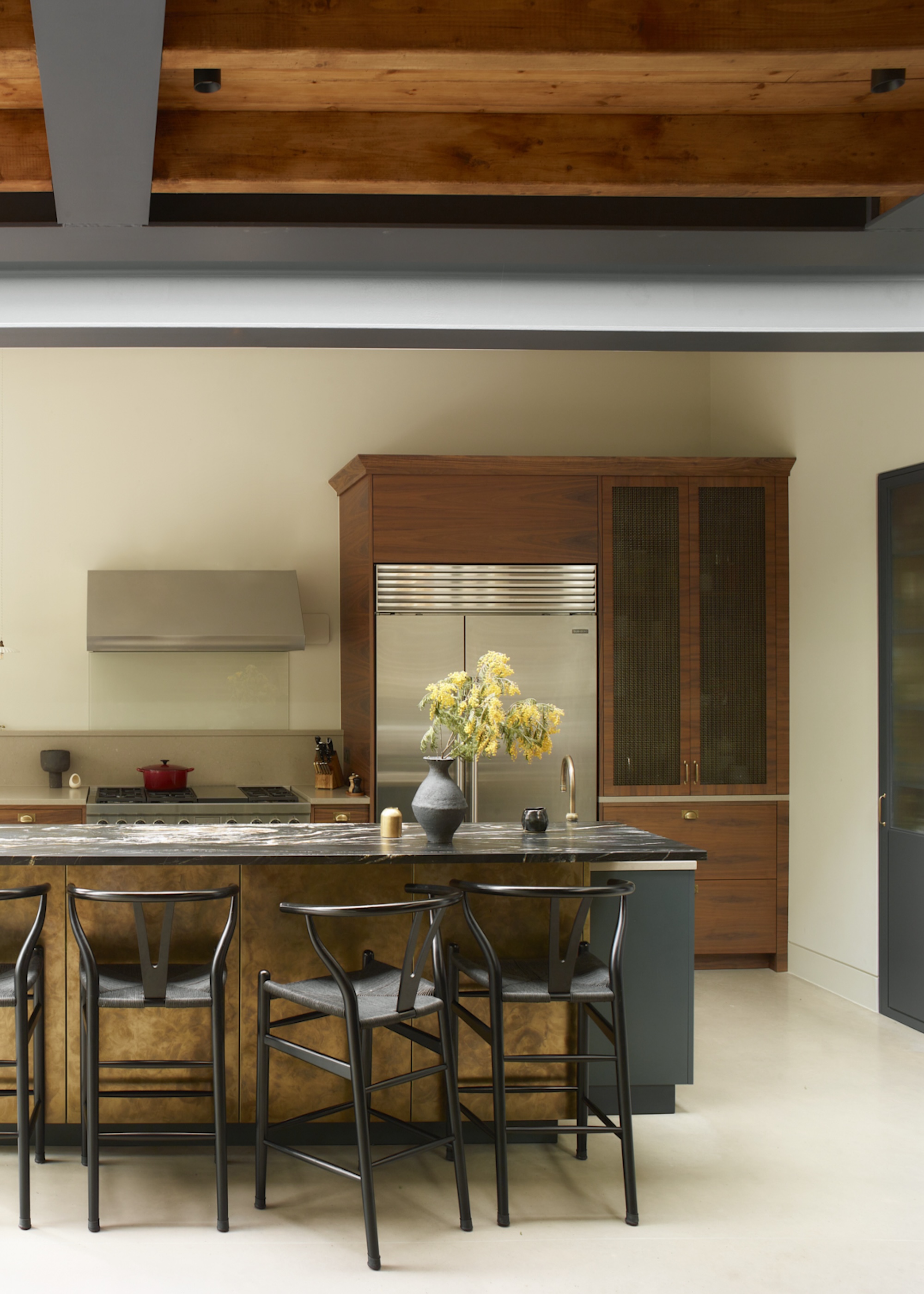 A dark wood kitchen with mesh kitchen door fronts on the cabinets next to the fridge. There is also a large island in the middle with dining chairs beside it