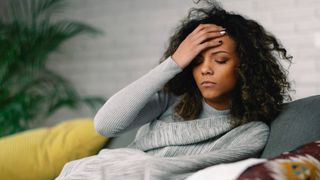 woman on couch holding head in pain