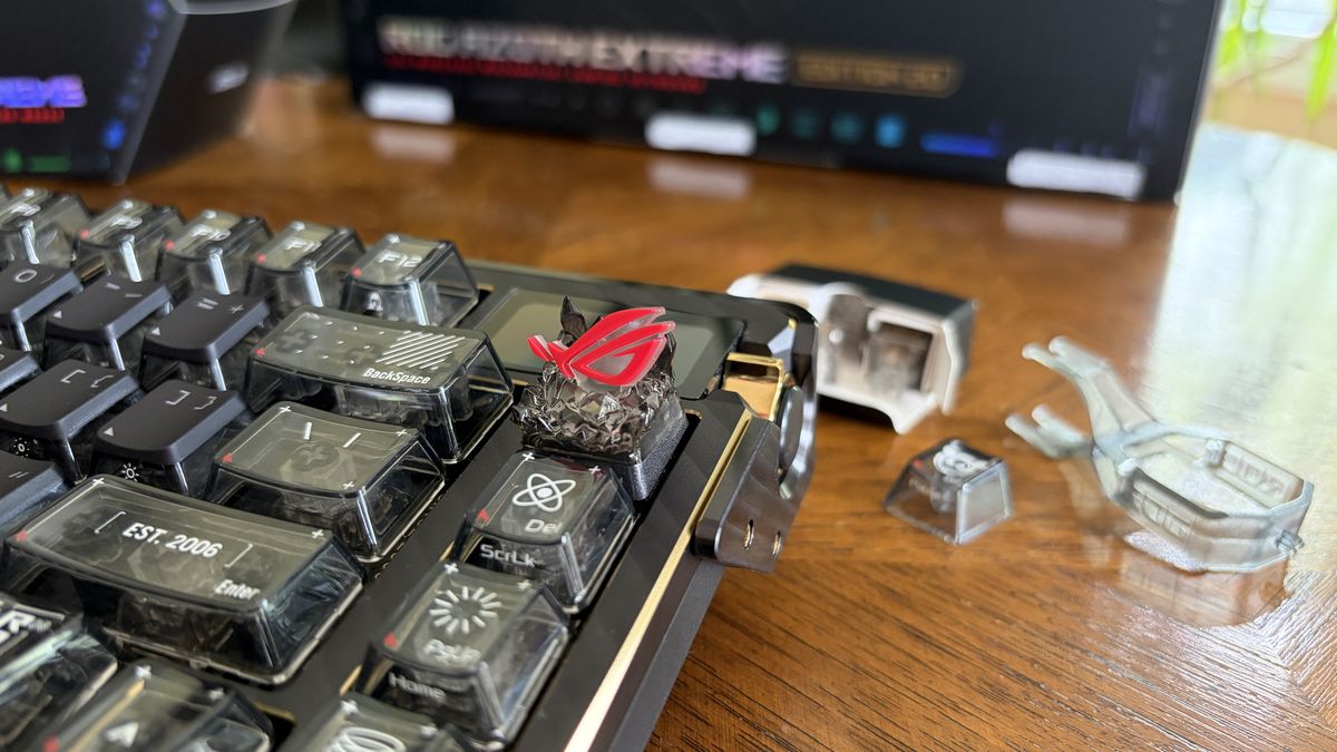 Close-up of an ASUS ROG mechanical keyboard with a decorative red keycap and tools on a wooden table.
