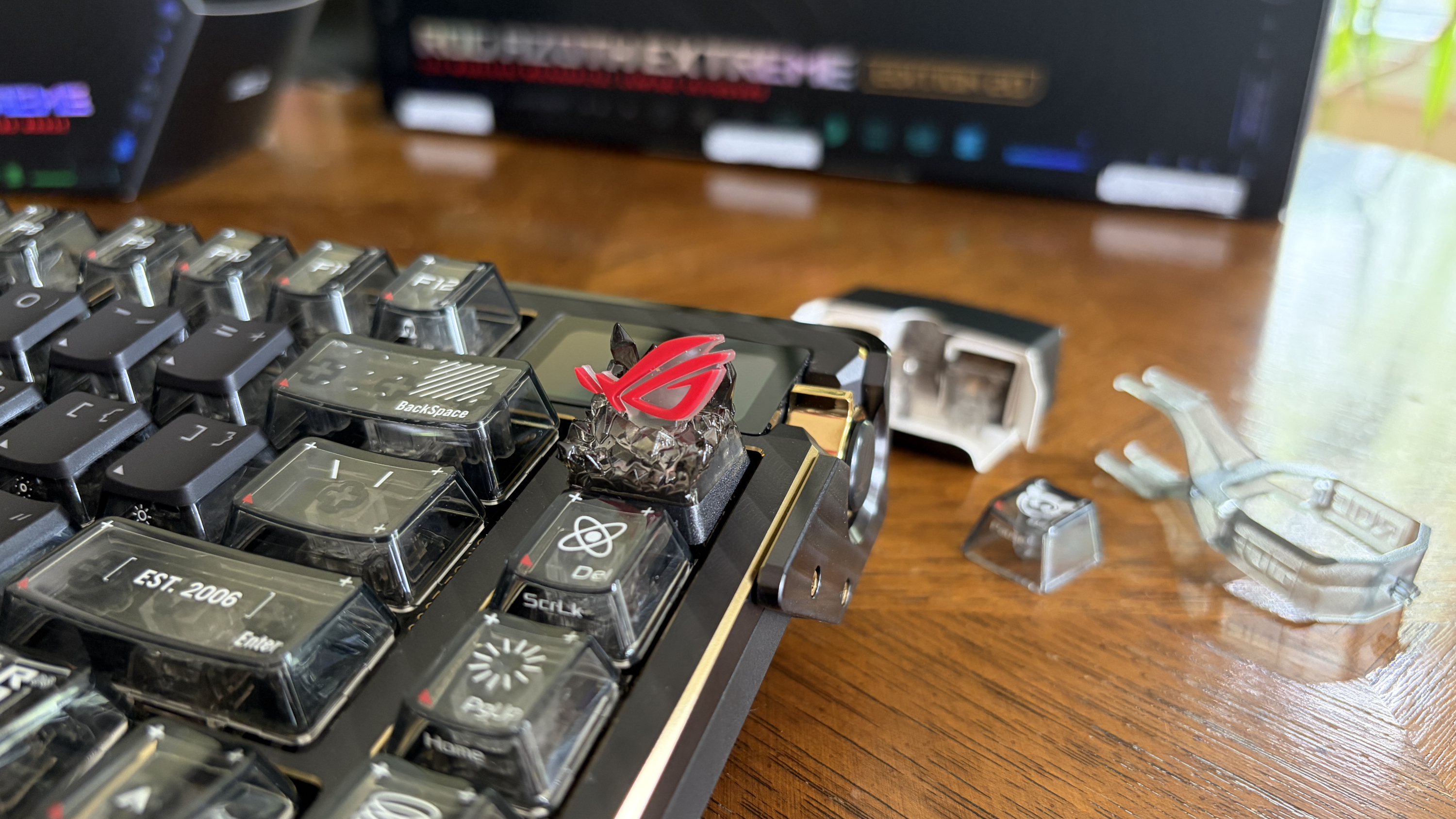 Close-up of an ASUS ROG mechanical keyboard with a decorative red keycap and tools on a wooden table.