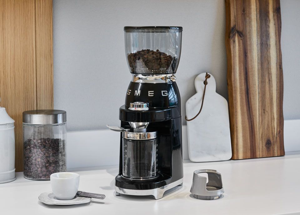 A black Smeg coffee grinder on a countertop in a modern kitchen