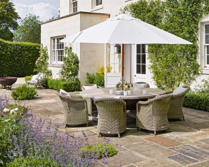 How to build a patio demonstrated in a large stone patio space with round table and white parasol.