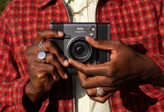 Fujifilm Instax Wide Evo instant camera in the user's hand who is adjusting the lens