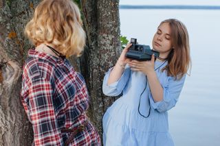 A photographer using a Polaroid camera to photograph a person standing against a tree