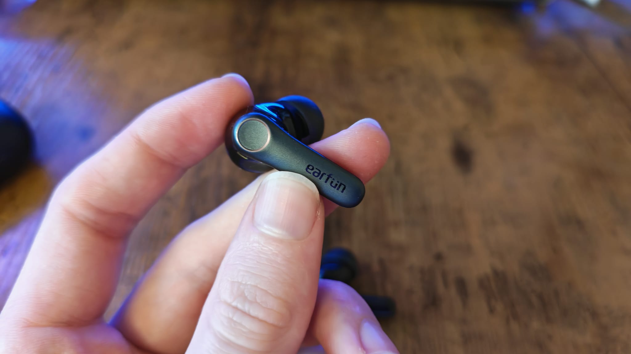 A reviewer holding one of the EarFun Air Pro 4, showing its touchpad