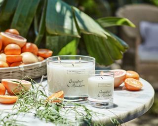 2 x The White Company Grapefruit & Mandarin Candles in different sizes styled in outdoor setting with citrus fruits around