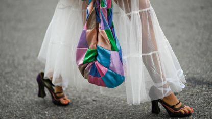 NEW YORK, NEW YORK - SEPTEMBER 13: A guest wears a pale pink / green / blue tie and dye print pattern square neck / long top, a white tulle ruffled skirt, a multicolored print pattern silk handbag, khaki suede cut-out block heels sandals, outside Gabriela Hearst, during New York Fashion Week, on September 13, 2022 in New York City. 