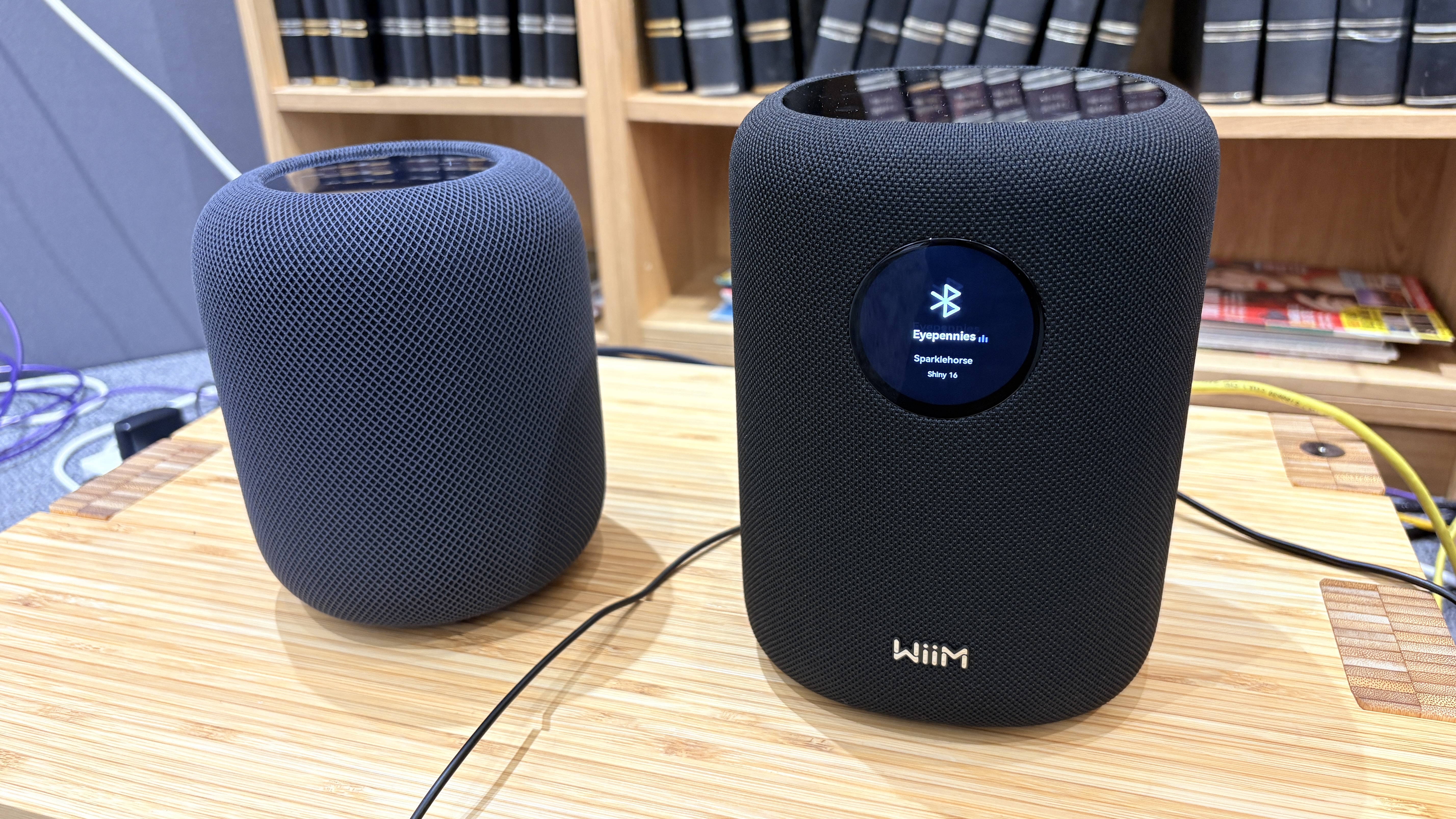 A black Apple HomePod 2 next to a black WiiM Sound on a wooden surface