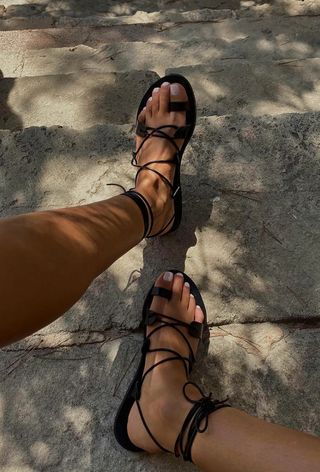 Black lace-up sandals with sheer white nail colour on toes